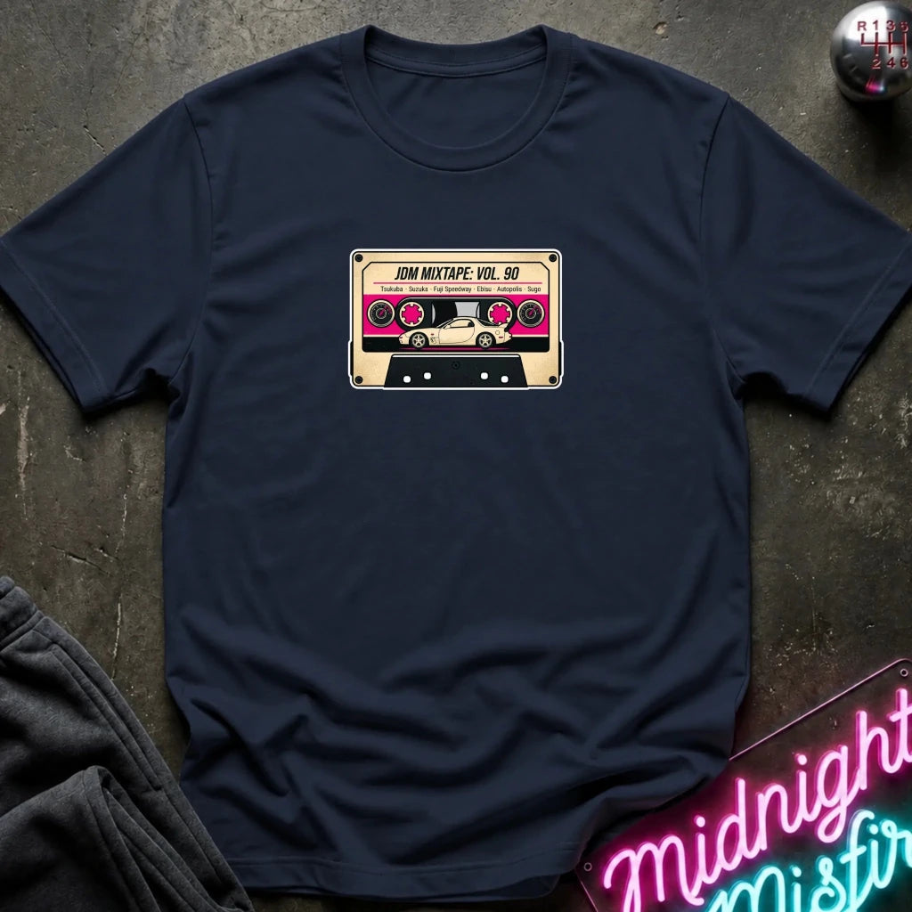 A navy blue crewneck t-shirt laid flat on a dark textured surface, featuring a retro cassette tape graphic on the chest with the text 'JDM MIXTAPE VOL.