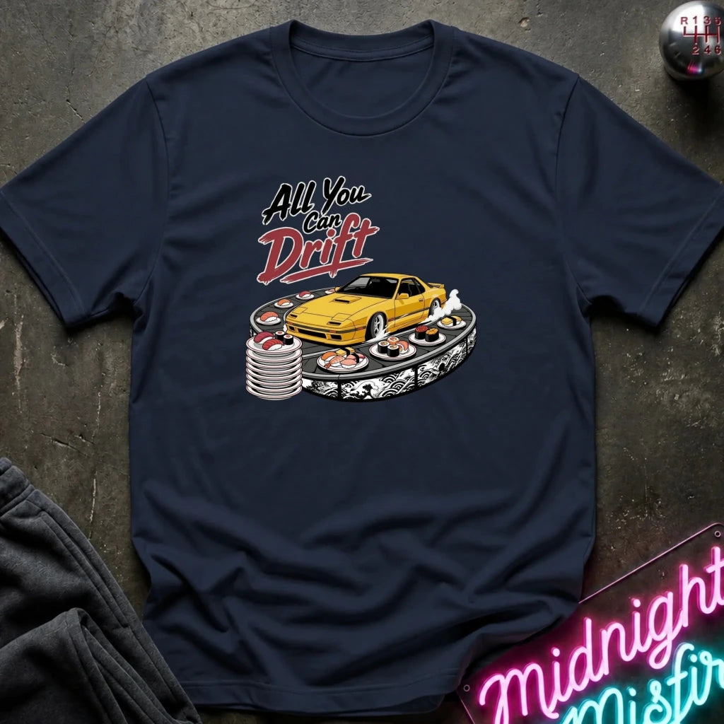 A navy blue graphic t-shirt laid flat on a dark textured surface. The graphic features a yellow sports car surrounded by sushi and stacks of poker chips, with the text 'All You Can Daft' in stylized white and red lettering.