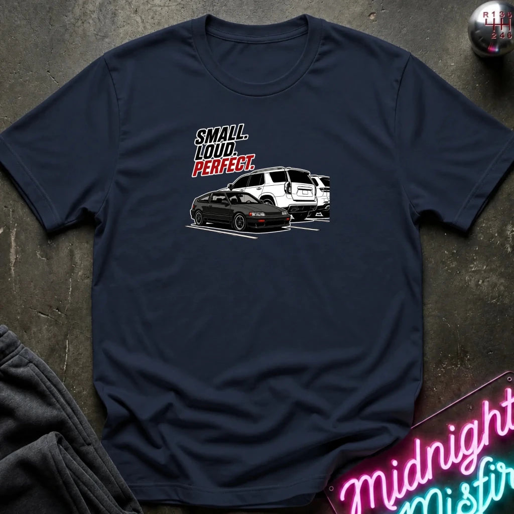 navy  short-sleeve graphic t-shirt laid flat on a dark textured surface. The graphic features the text 'SMALL louD PERFECT.