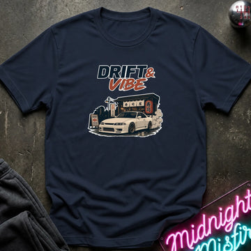 A navy blue graphic t-shirt laid flat on a dark textured surface. The shirt features a graphic print of a white sports car with smoke effects and the text 'DRIFT & VIBE' in stylized lettering.