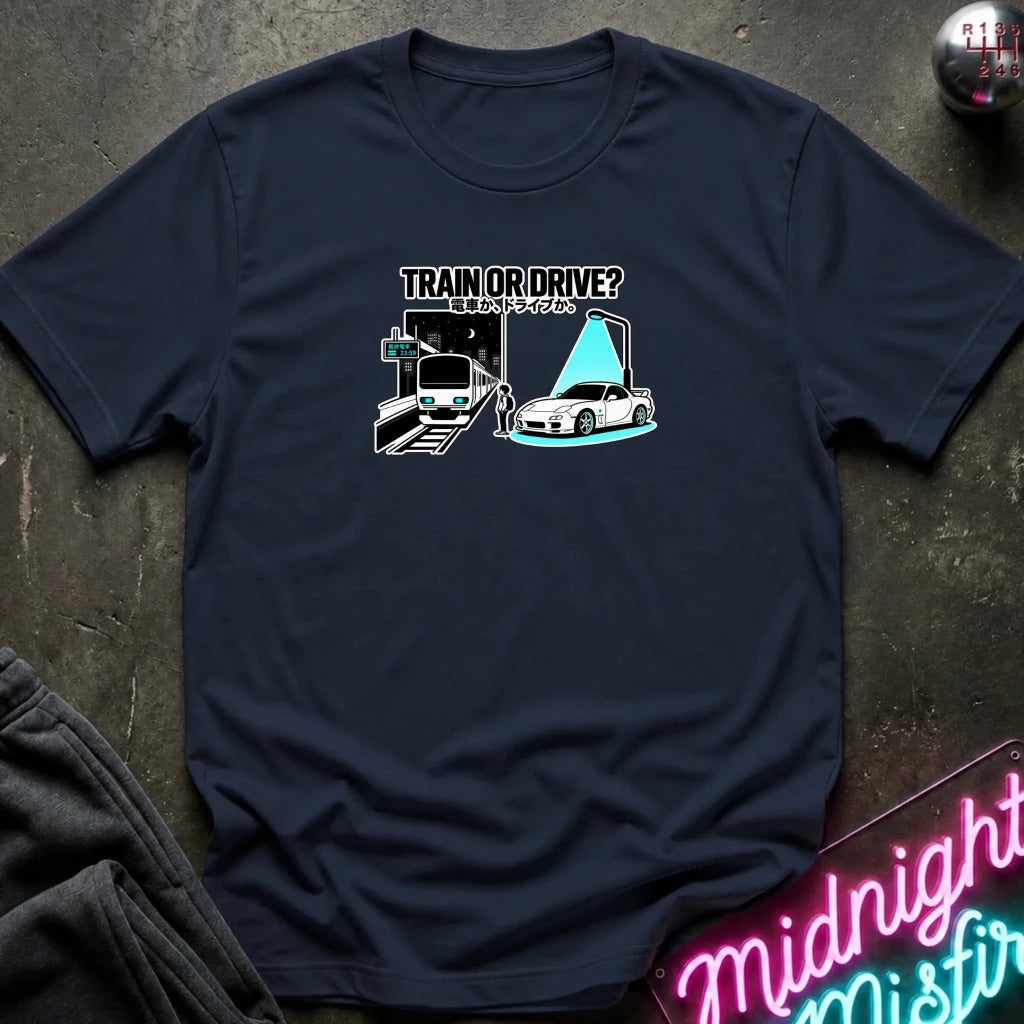 navy graphic t-shirt laid flat on a dark textured surface. The graphic features a train and a car with a person.