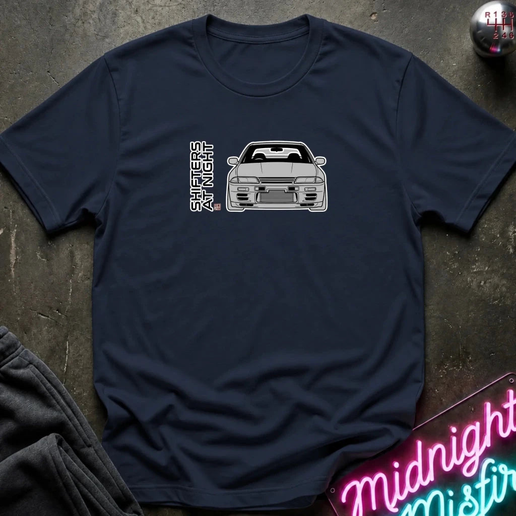 A navy blue short-sleeve t-shirt laid flat on a dark textured surface, featuring a white line-art graphic of a sports car and the vertical text 'SHOOTERS' on the chest. 