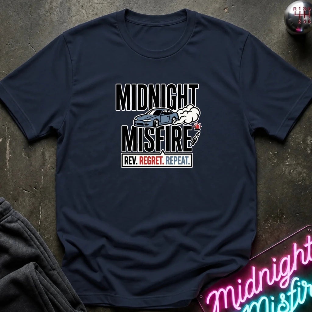 A navy blue graphic t-shirt laid flat on a dark textured surface. The shirt features a white and red graphic print with the text 'MIDNIGHT MISFIRE' and 'REV.