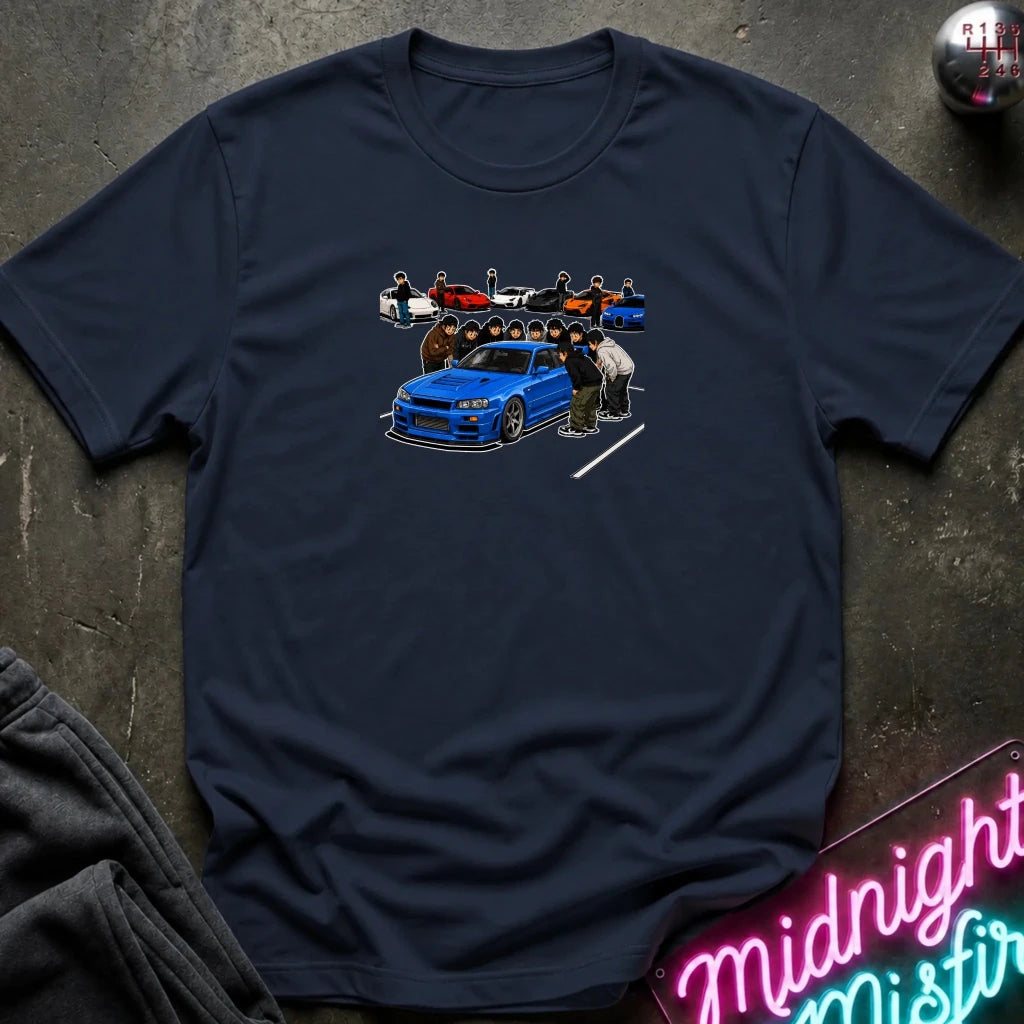 A navy blue short-sleeve t-shirt laid flat on a dark textured surface, featuring a colorful graphic print of a blue sports car and several anime-style characters.