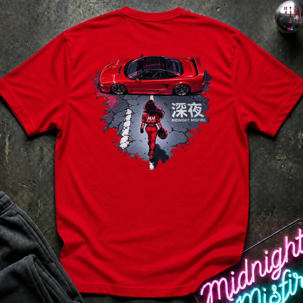 A bright red short-sleeve graphic T-shirt laid flat on a dark textured surface. The shirt features a large back print showing a red sports car above a red racer in a splattered gray and black design
