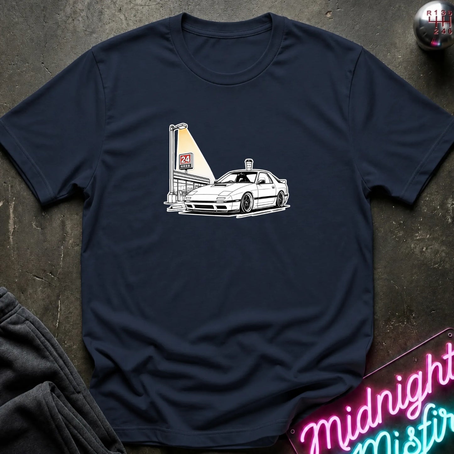 A navy blue short-sleeve crewneck t-shirt laid flat on a dark textured surface, featuring a black line art graphic of a white sports car parked next to a lit street lamp.
