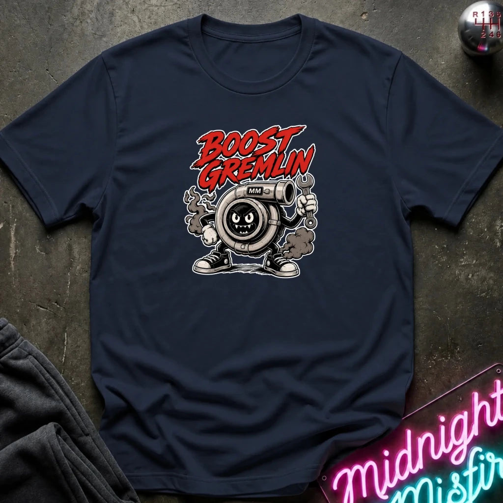 A navy blue graphic t-shirt laid flat on a dark textured surface. The shirt features a cartoon illustration of a turbocharger character with the text 'BOOST GREMLIN' in red and white.