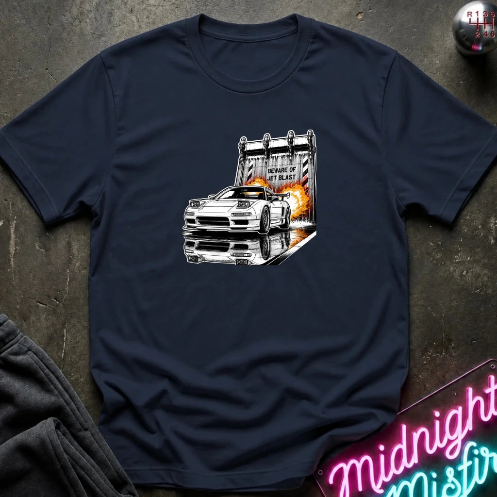 A navy blue short-sleeve t-shirt laid flat on a dark textured surface, featuring a graphic print of a white sports car in front of a blast off area.