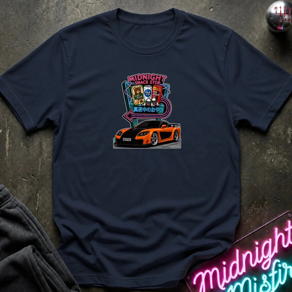A navy blue  short-sleeve t-shirt laid flat on a dark textured surface, featuring a colorful graphic print of an orange sports car in front of a neon sign that reads 'Midnight Snack Stop'.
