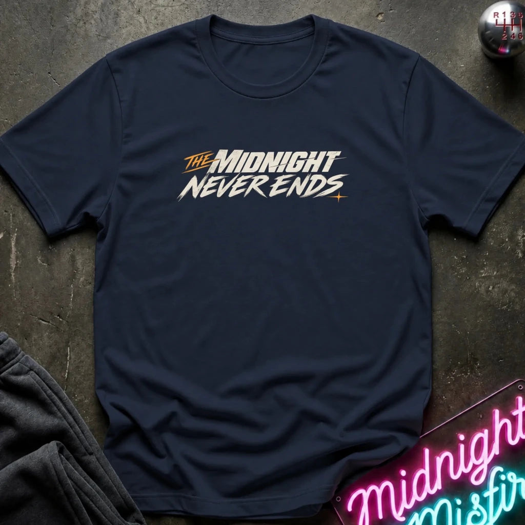 A navy blue short-sleeve t-shirt with a stylized graphic reading 'THE MIDNIGHT NEVER ENDS' across the chest, laid flat on a dark textured surface with a neon sign and folded dark fabric nearby.