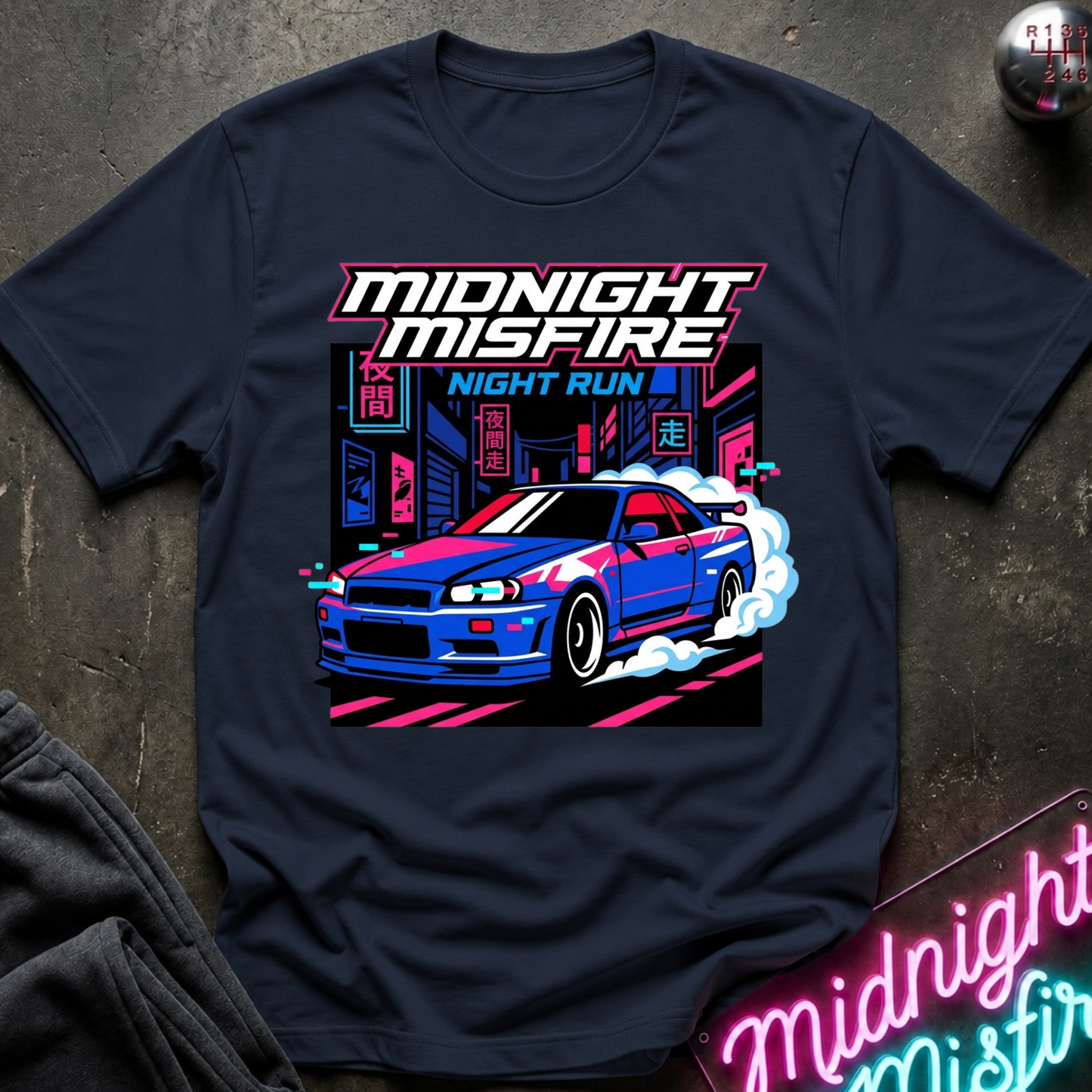 A navy blue graphic t-shirt featuring a vibrant neon-style print of a blue and white sports car with the text 'MIDNIGHT MISFIRE' and 'NIGHT RUN'. The shirt is styled flat on a dark textured surface with a neon sign and dark sweatpants partially visible.