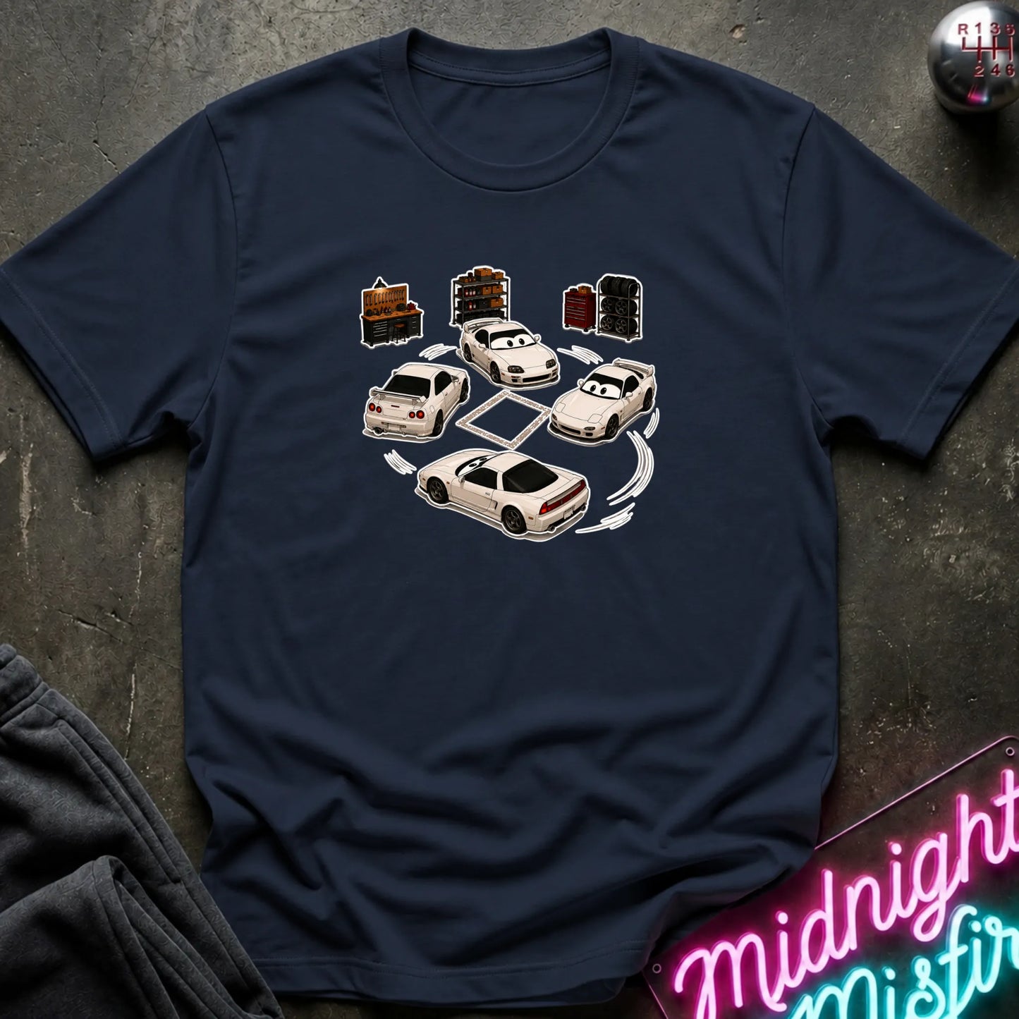 A navy blue short-sleeve t-shirt laid flat on a dark textured surface, featuring a graphic print of several white sports cars arranged in a circle with drift-like tire marks.