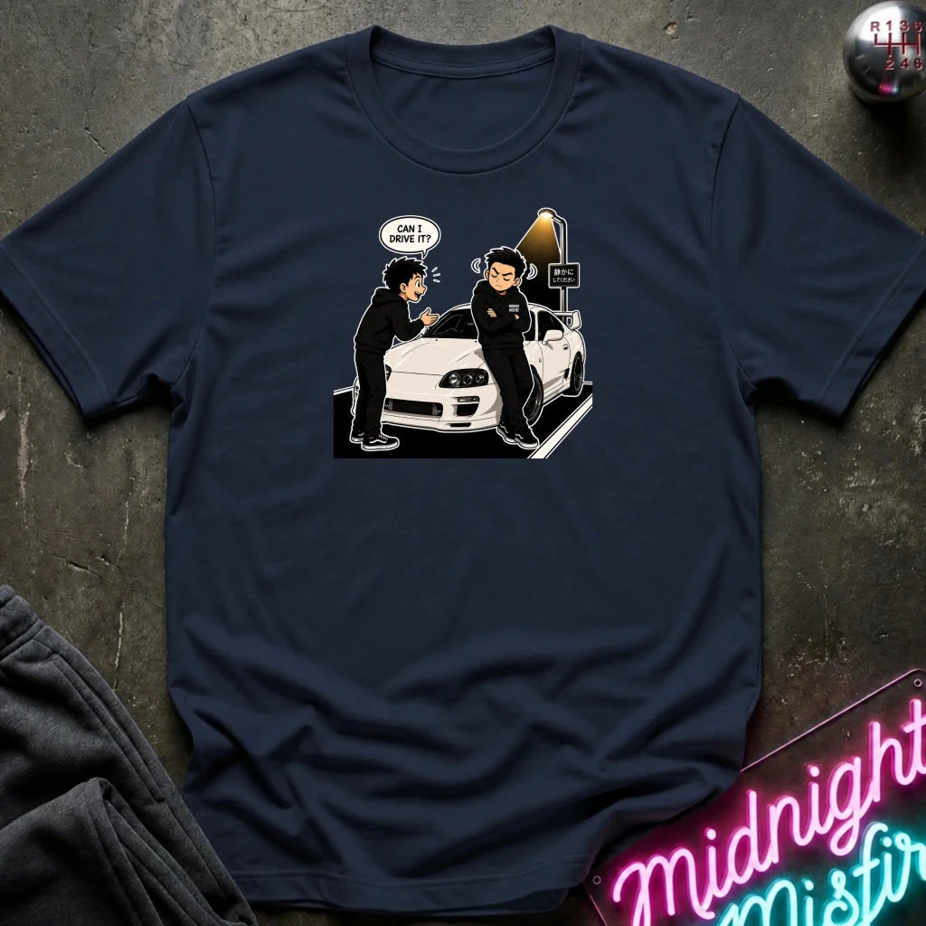A navy blue graphic t-shirt laid flat on a dark textured surface. The graphic shows a white sports car with two cartoon figures and a speech bubble 