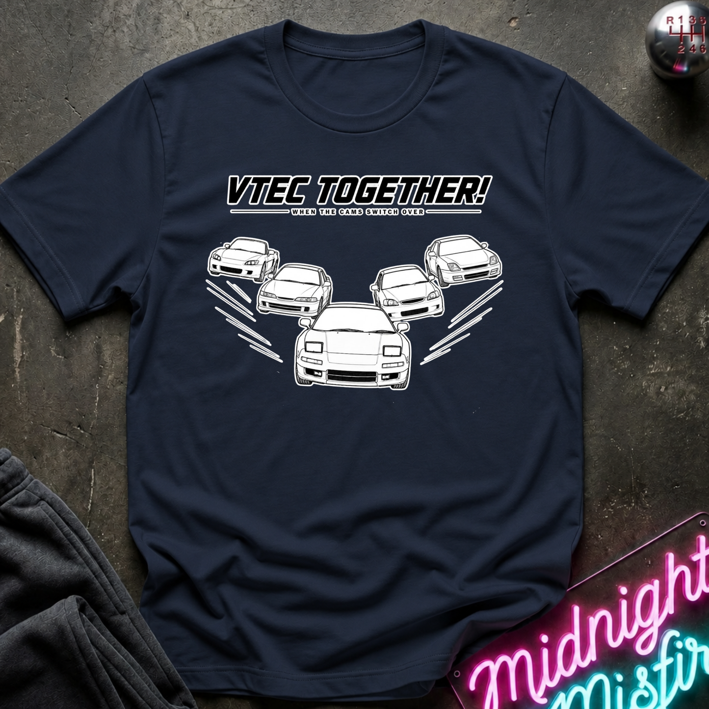 A navy blue graphic t-shirt laid flat on a dark textured surface. The shirt features a white graphic of several cars with the text 'VTEC TOGETHER!' printed on the chest.