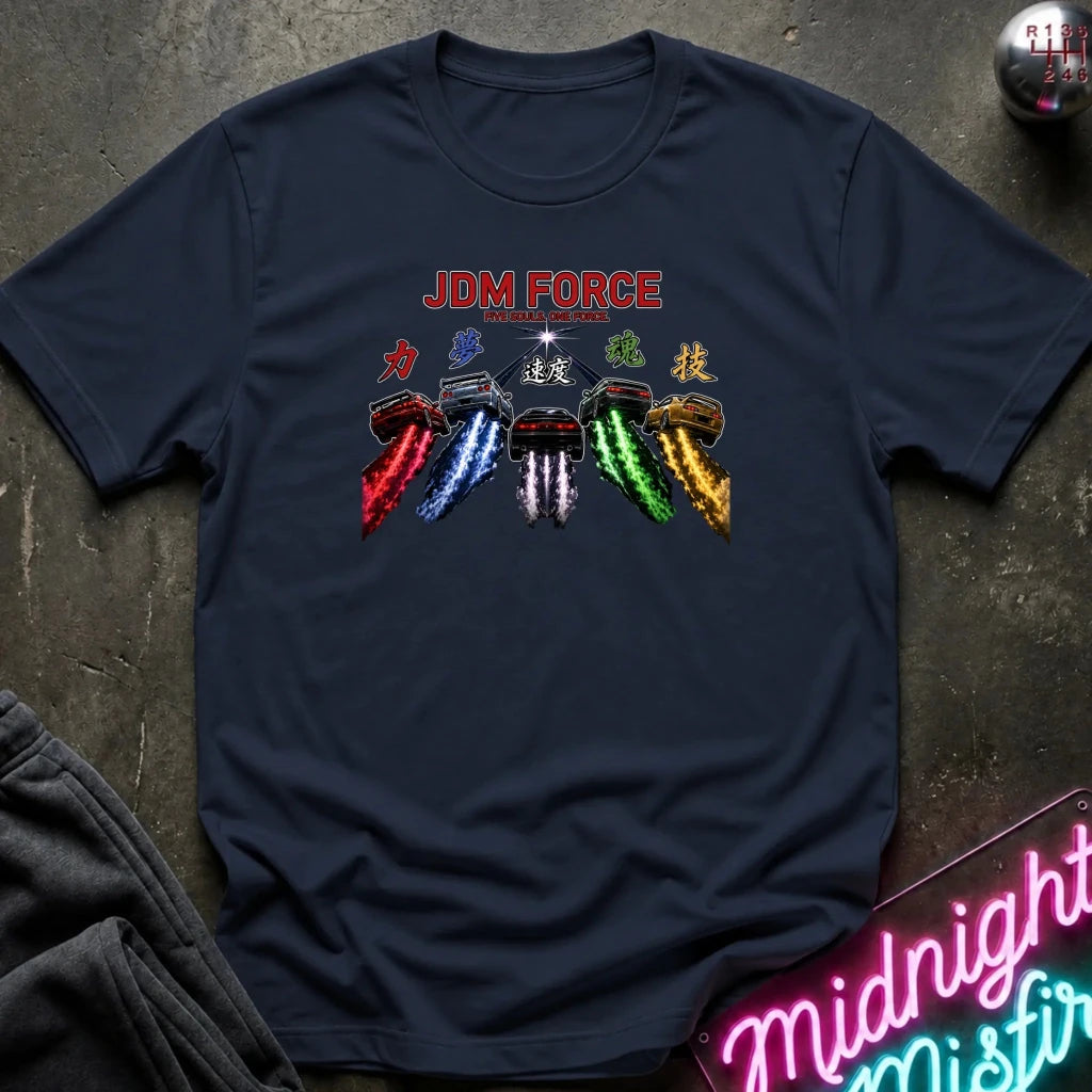A navy blue graphic t-shirt laid flat on a dark textured surface. The graphic features the text 'JDM FORCE' in red, above a row of classic cars with colorful smoke trails in red, blue, white, green, and gold.