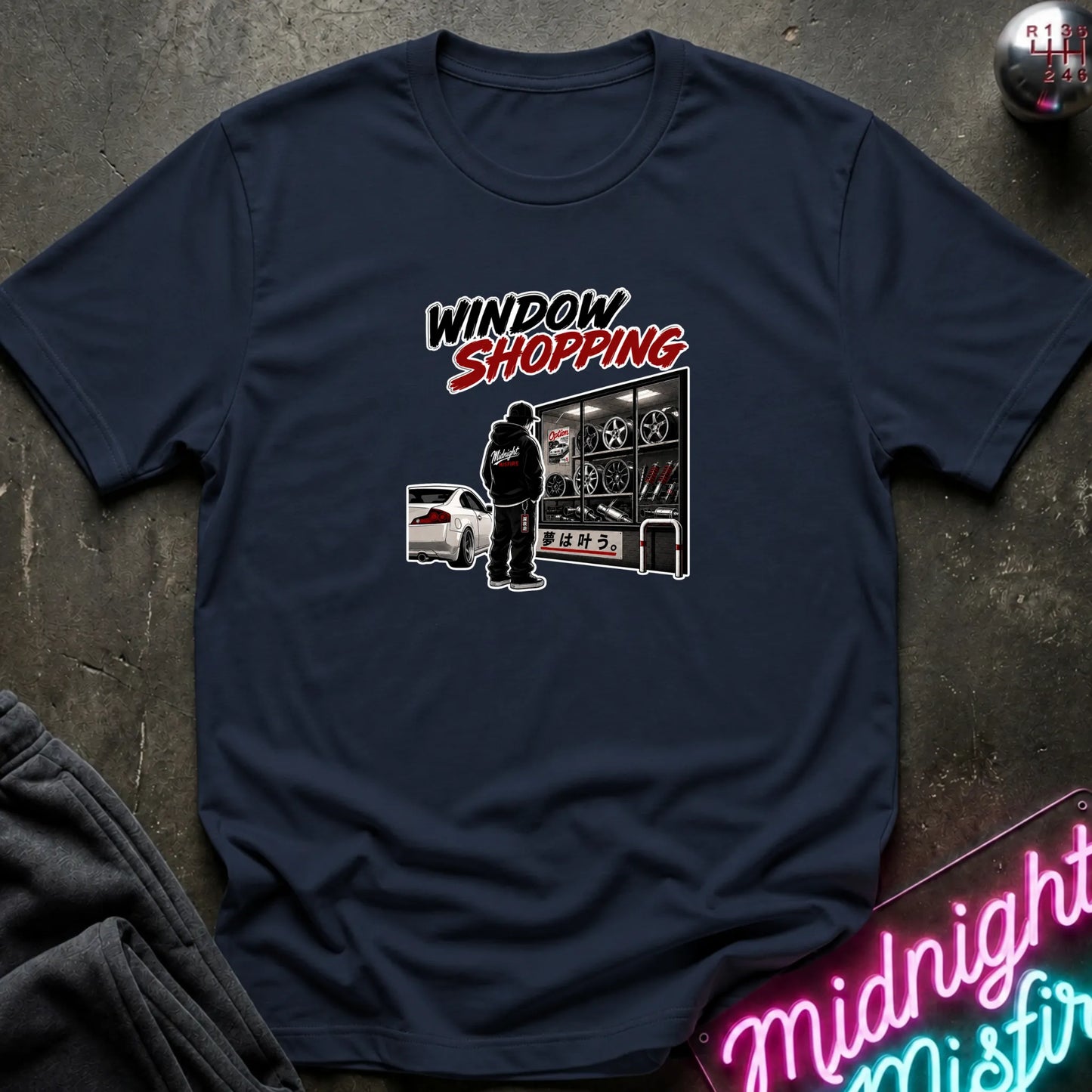 A navy short-sleeved t-shirt  that has a cars parked and a person checking out windows of parts.
