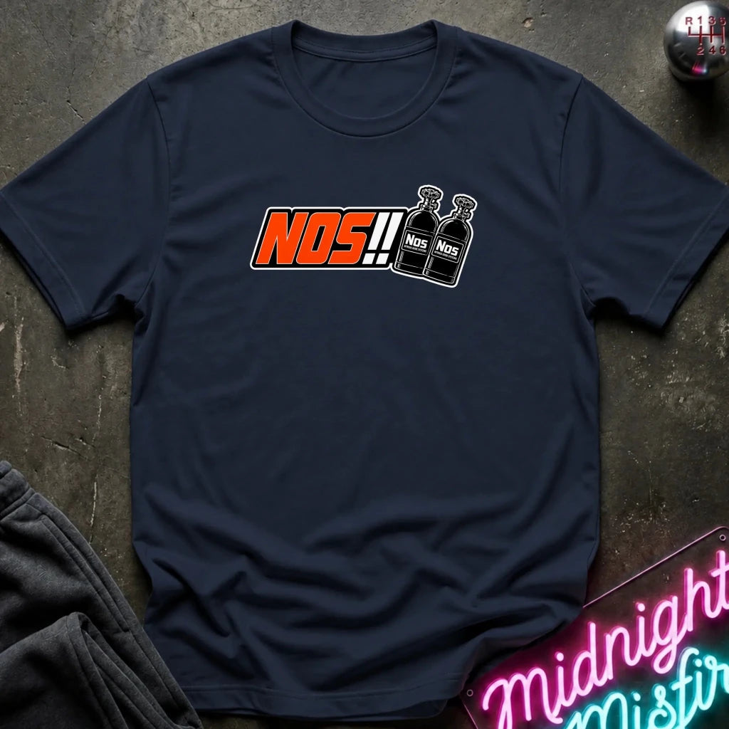 A navy blue t-shirt laid flat on a dark textured surface, featuring a graphic print of the word 'NOS!!' in orange and white next to two black bottles labeled 'NOS'.