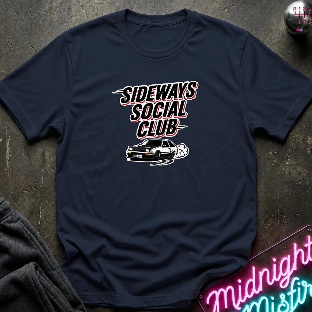 A navy blue graphic t-shirt laid flat on a dark textured surface. The shirt features a graphic print that reads 'SIDEWAYS SOCIAL CLUB' in stylized white and red lettering above a black car with white smoke.