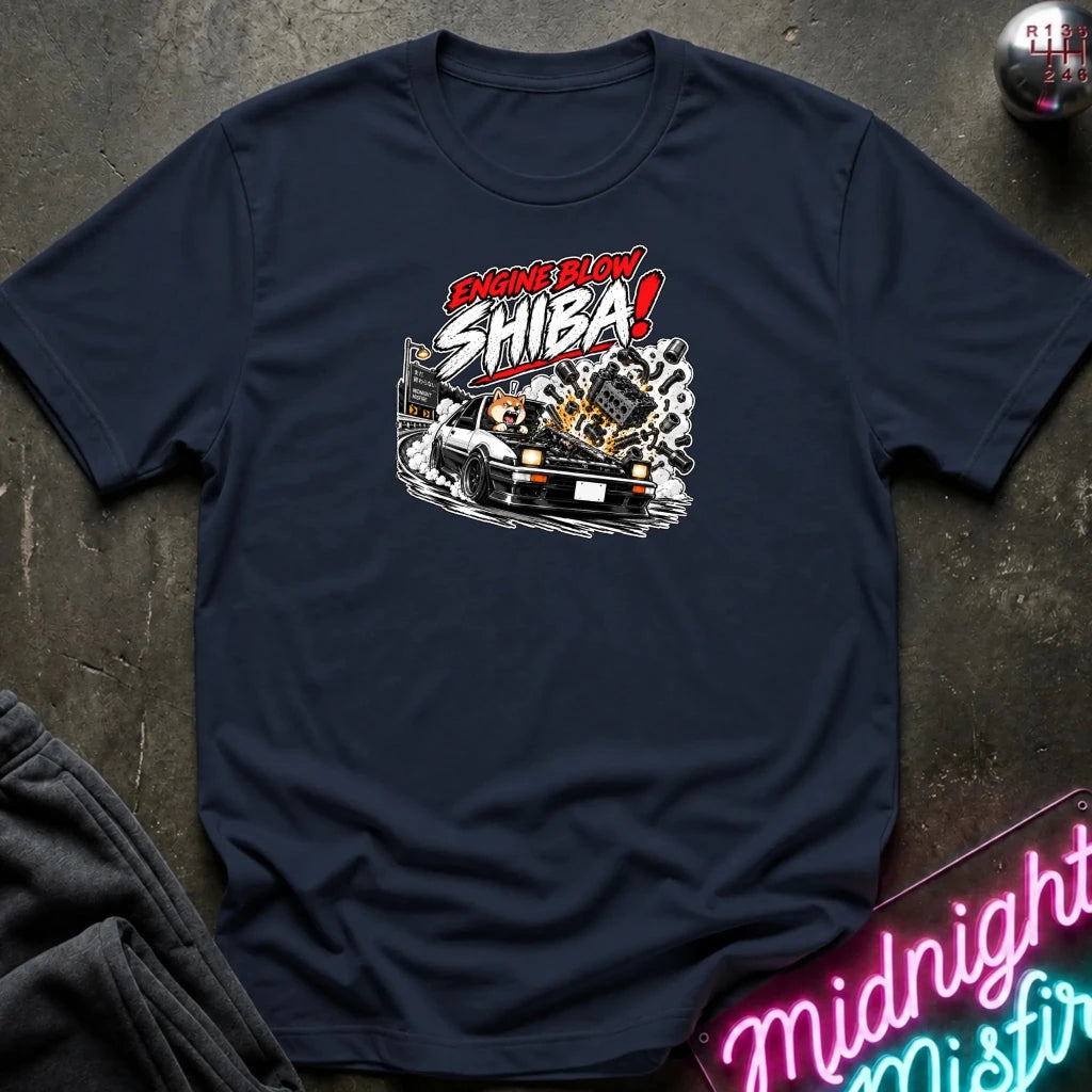 A navy blue short-sleeve graphic t-shirt laid flat on a dark textured surface. The shirt features a stylized graphic of a white sports car with a glowing engine and the text 'ENGINE BLOW SHIBA!' in red, white, and black.