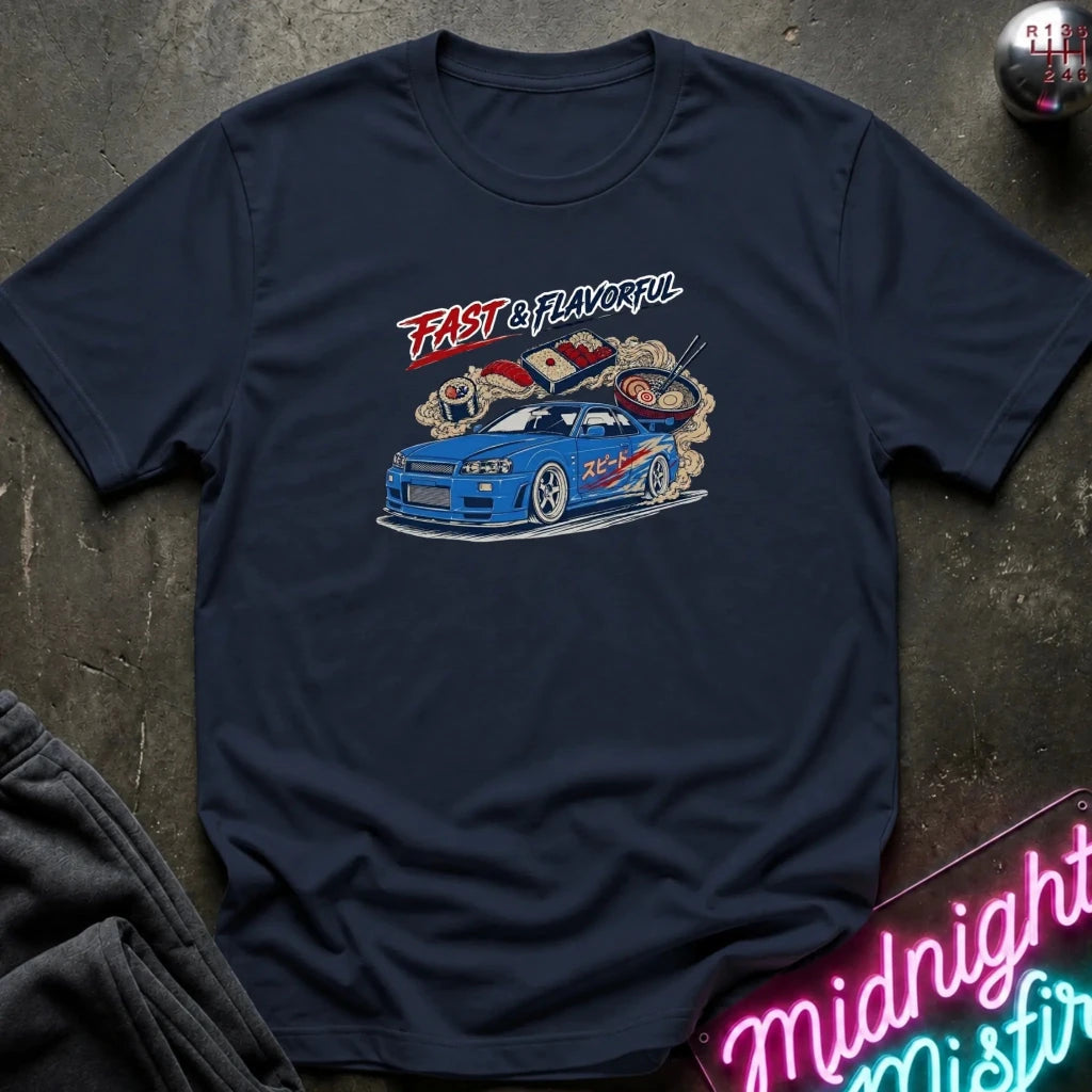 A navy blue short-sleeve t-shirt with a graphic print of a blue sports car and the words 'FAST & FLAVORFUL' in red and white, laid flat on a dark textured surface.