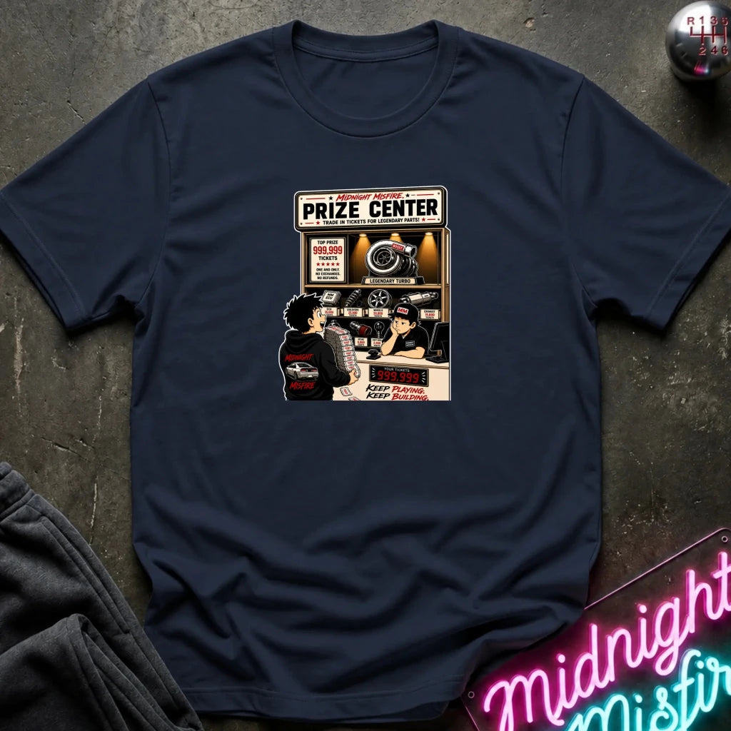 A navy blue  short-sleeve crewneck t-shirt laid flat on a dark textured surface, featuring a vintage-style graphic print of a 'Prize Center' with illustrated characters and neon signs in the background.