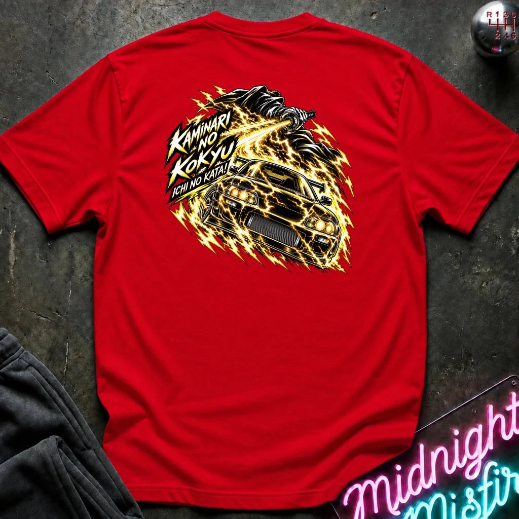 A red short-sleeve t-shirt laid flat on a dark textured surface, showing the back graphic with a car and the text "ichi no kata!"