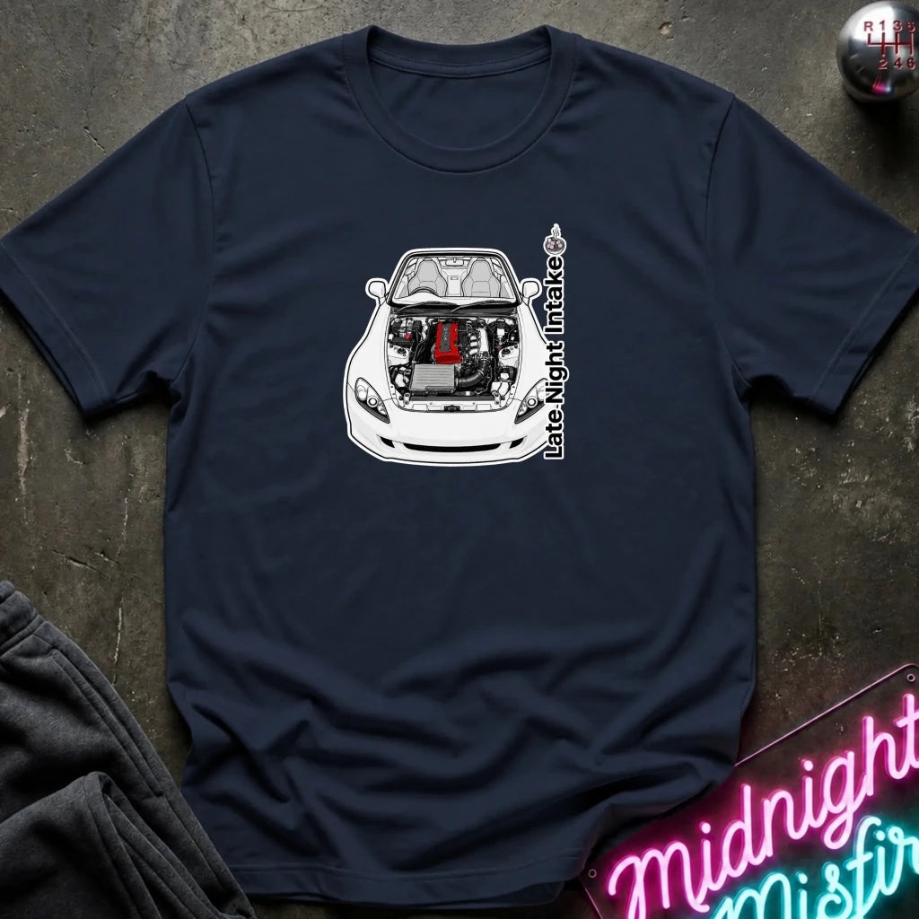 A navy blue short-sleeve t-shirt laid flat on a dark textured surface, featuring a graphic of a white sports car with its hood open, revealing a red engine component, alongside the vertical text 'Late Night Intake'.