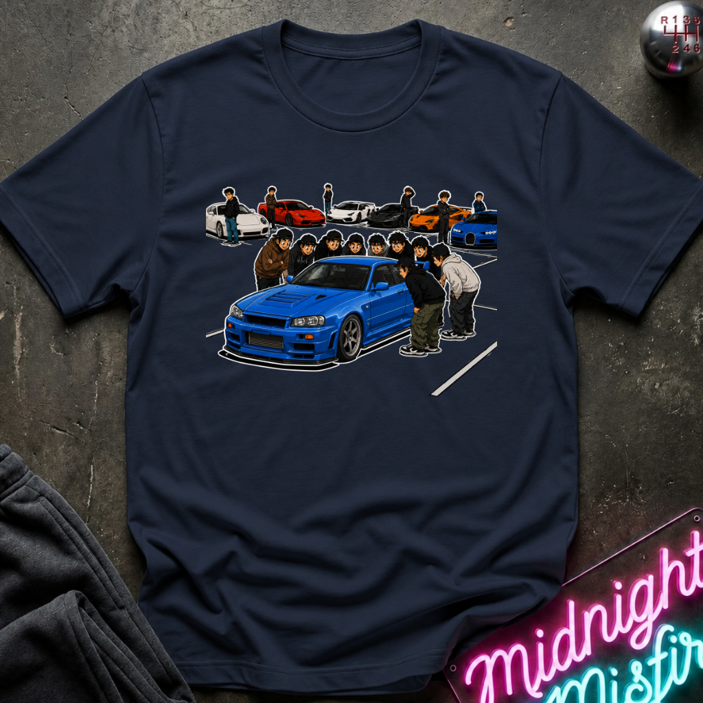 A navy blue graphic t-shirt laid flat on a dark textured surface. The shirt features a detailed graphic print of a blue sports car and several illustrated people.