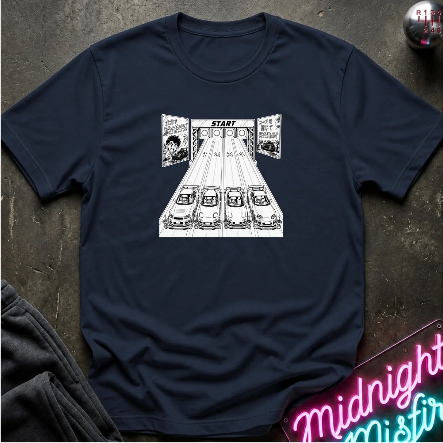 A navy blue short-sleeve t-shirt laid flat on a dark textured surface, featuring a black-and-white graphic of 4 cars lined up at a racing on a track.