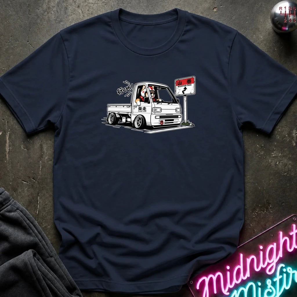 A navy blue crewneck t-shirt laid flat on a dark textured surface, featuring a graphic of a white classic pickup truck with a driver and a street sign. 