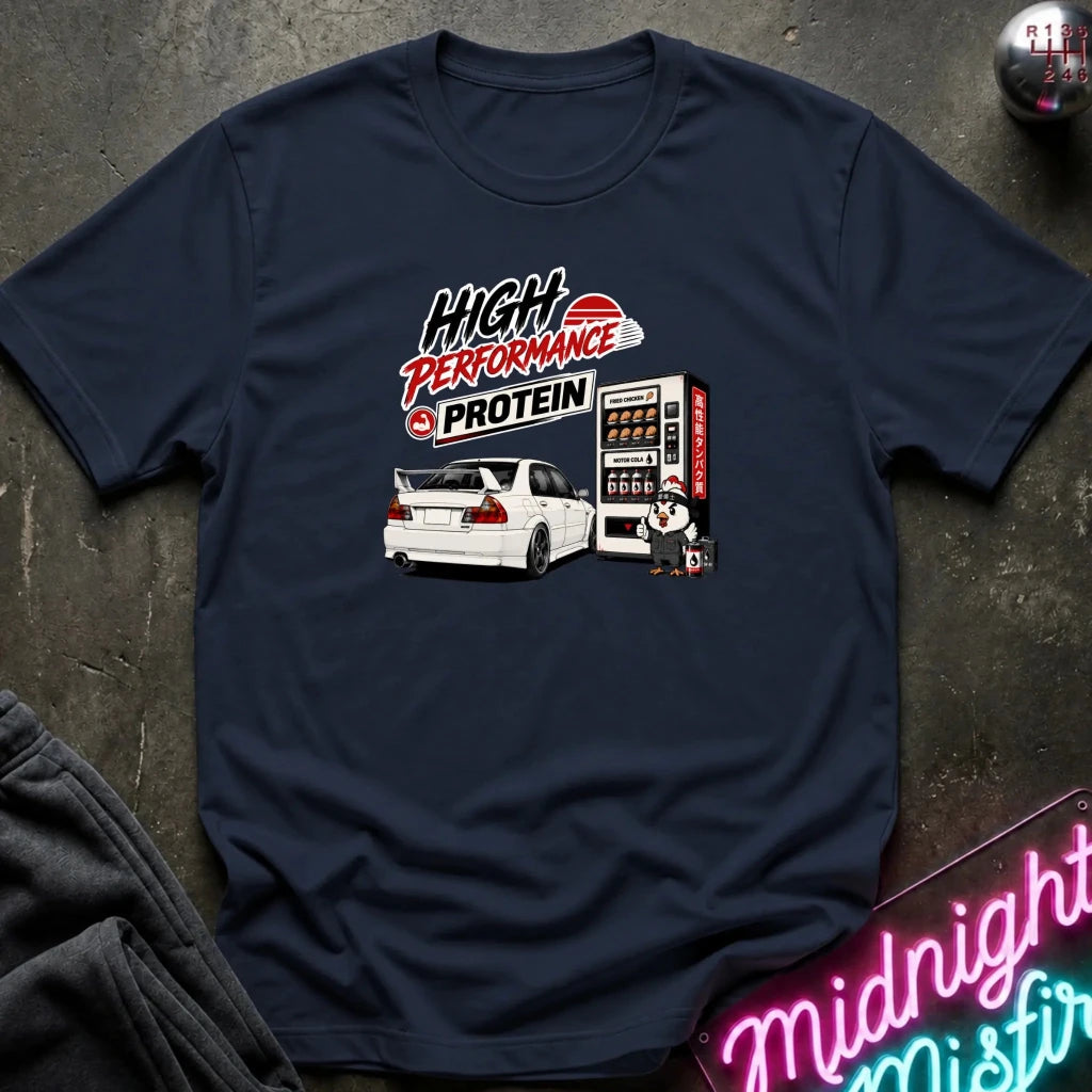 A navy blue short-sleeve graphic T-shirt laid flat on a dark textured surface. The shirt features a printed design with the text 'HIGH PERFORMANCE PROTEIN' above an illustration of a white sports car next to a vending machine.