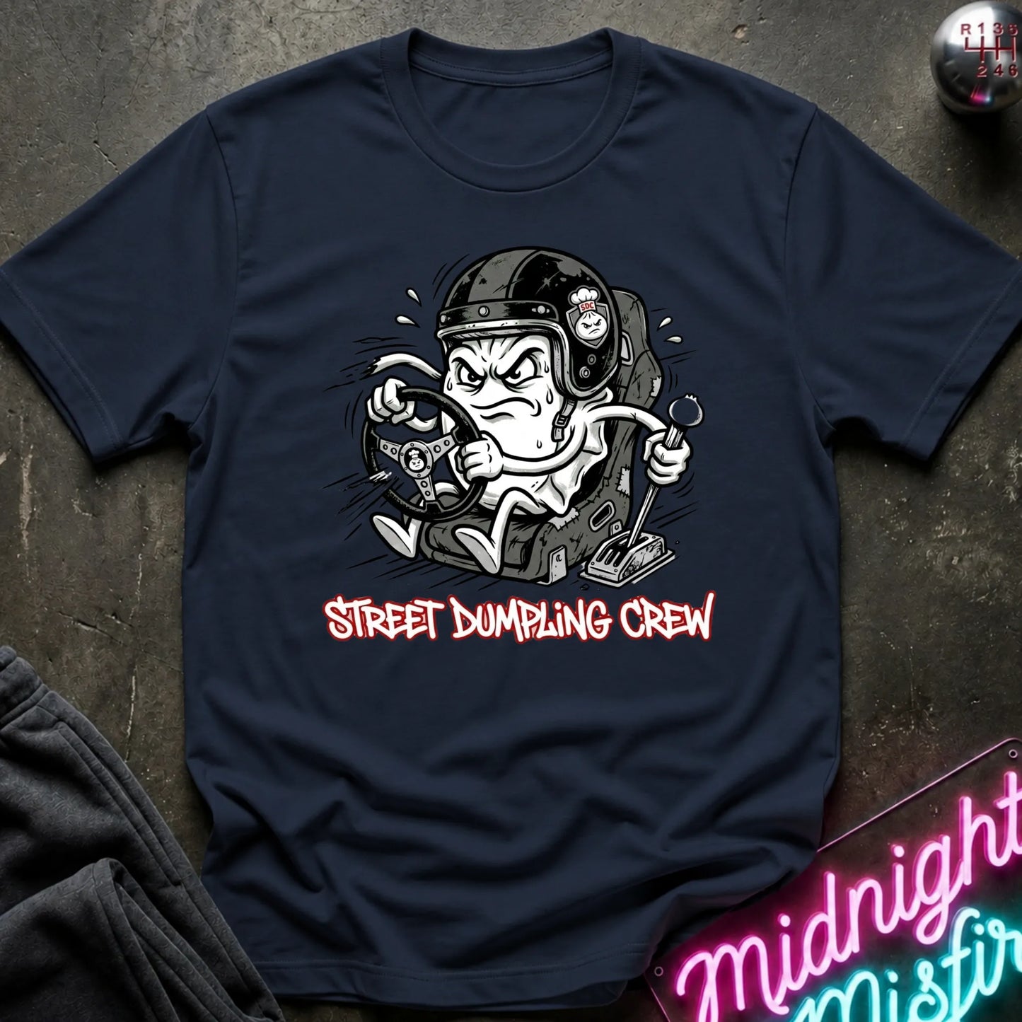 A navy blue graphic t-shirt laid flat on a dark textured surface. The shirt features a cartoon illustration of a street-dumping character in a helmet with the text 'STREET DUMPING CREW' printed below in red and white.