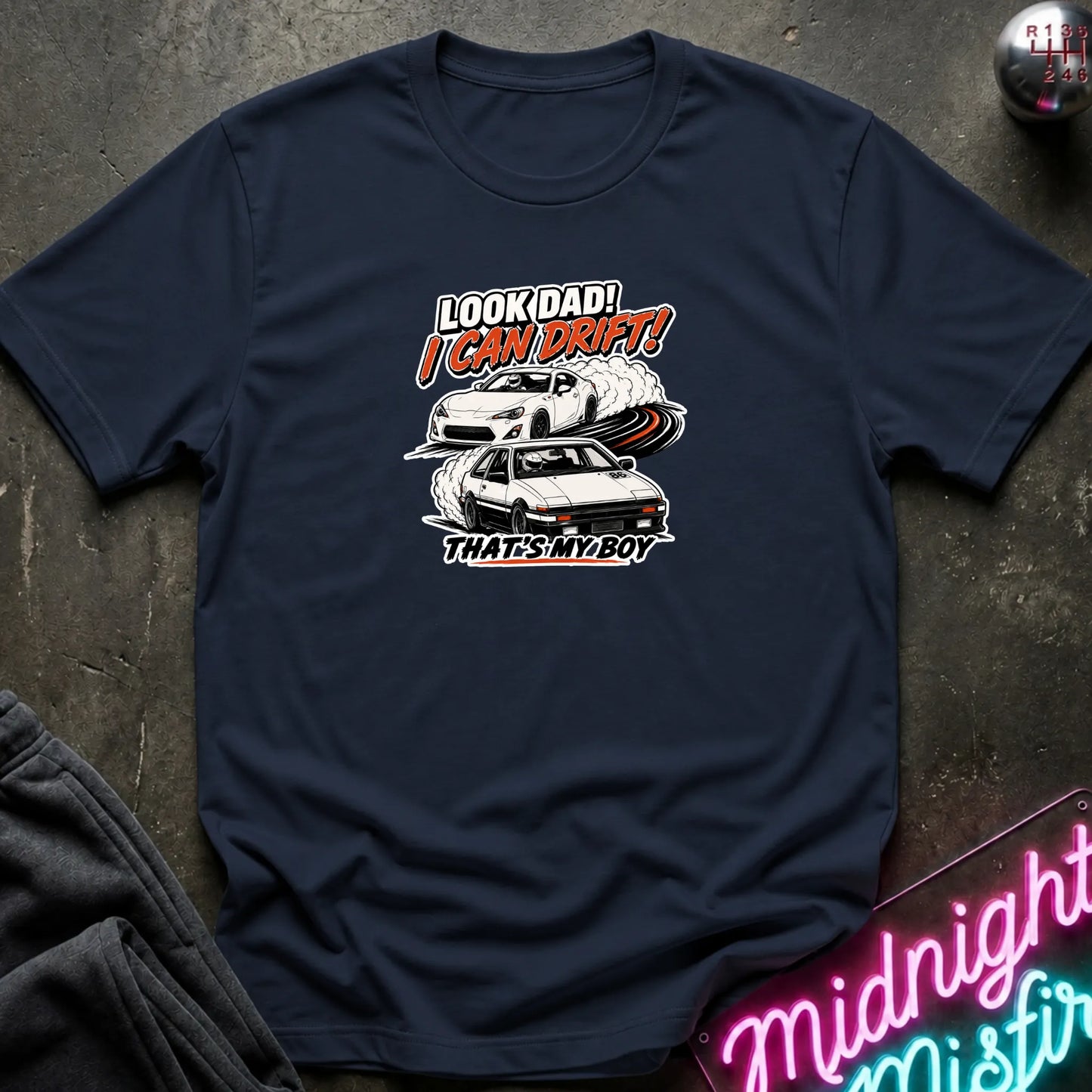 A navy  short-sleeved t-shirt  that has a cars drifting which are older and newer generations of toyotas.