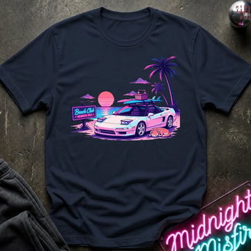 A navy blue graphic t-shirt laid flat on a dark textured surface. The graphic features a retro neon sunset scene with a pink and white sports car, palm trees, and a 'Beach Club' sign.