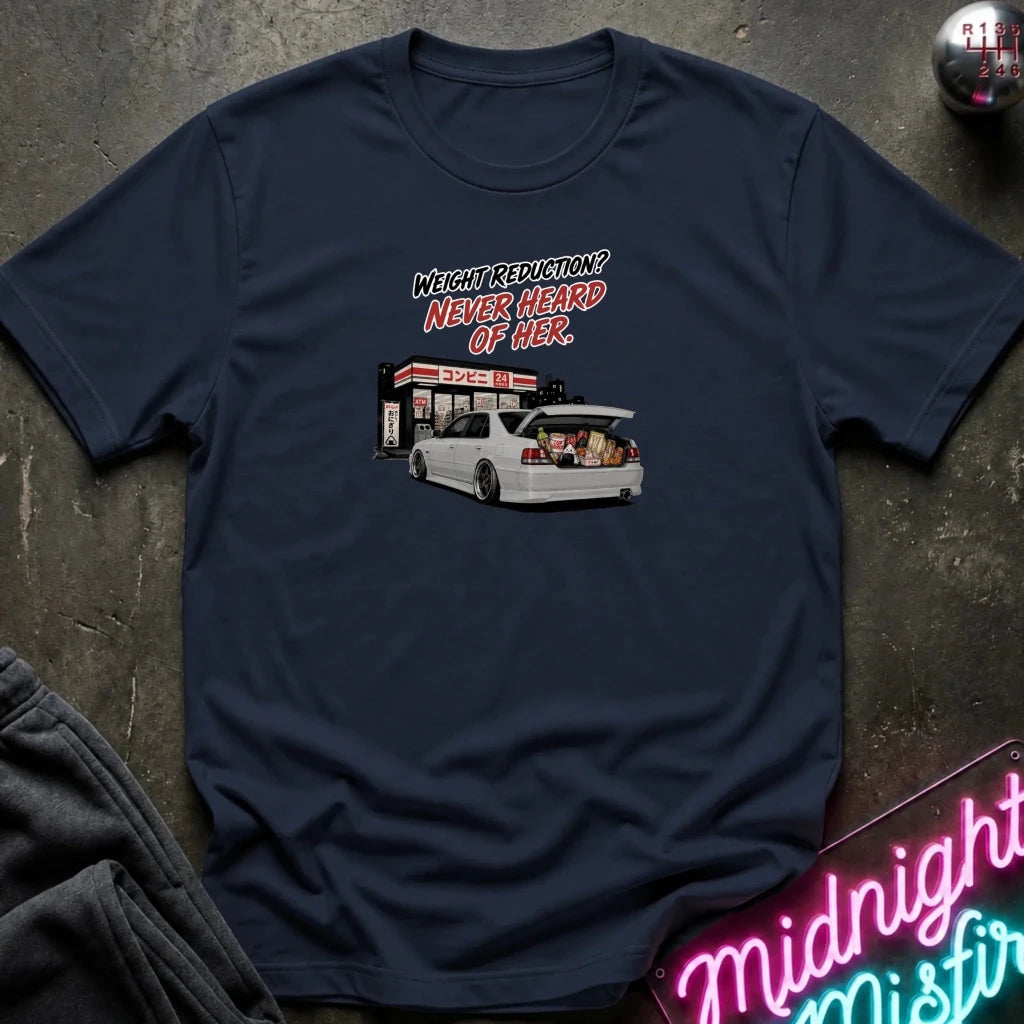A navy blue graphic t-shirt laid flat on a dark textured surface. The graphic features a white station wagon with its trunk open, parked 