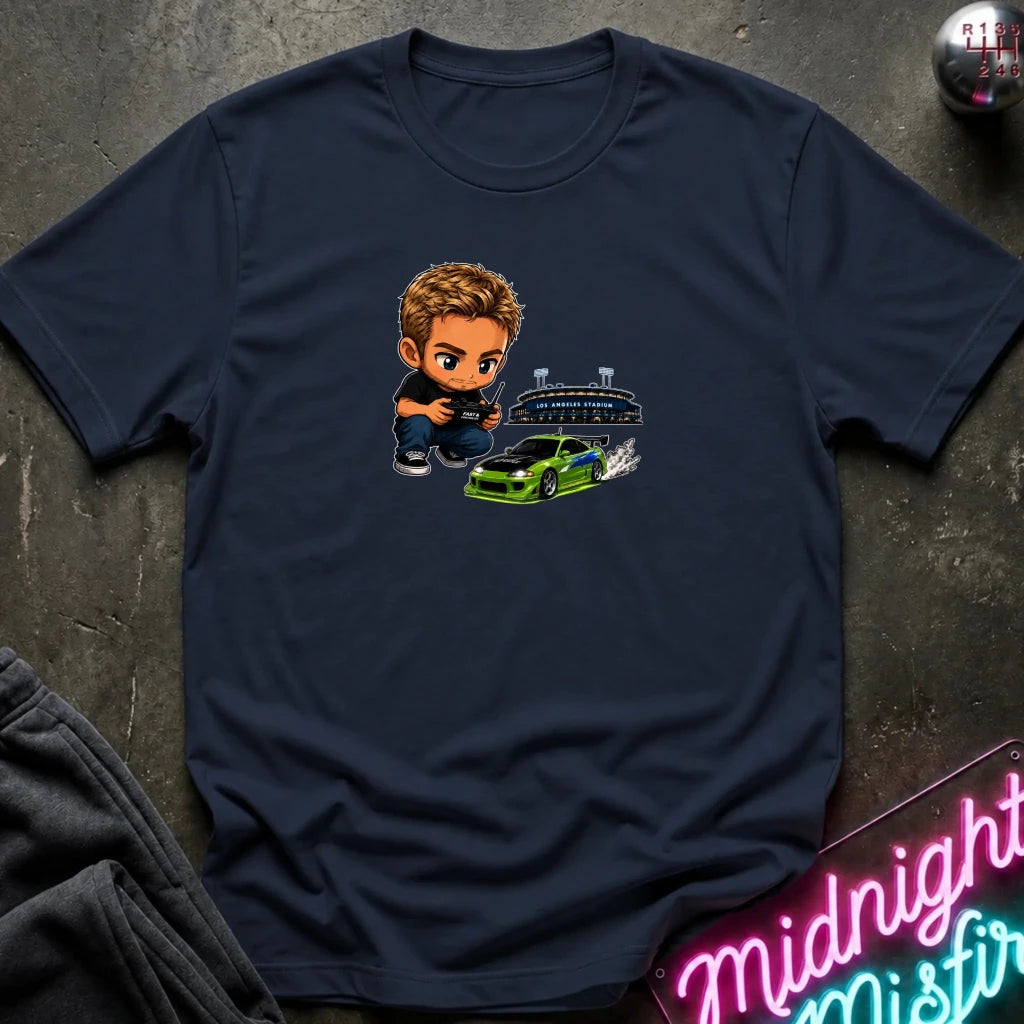 A navy graphic t-shirt laid flat on a dark textured surface. The graphic features a green car, and person  controlling it with remote.