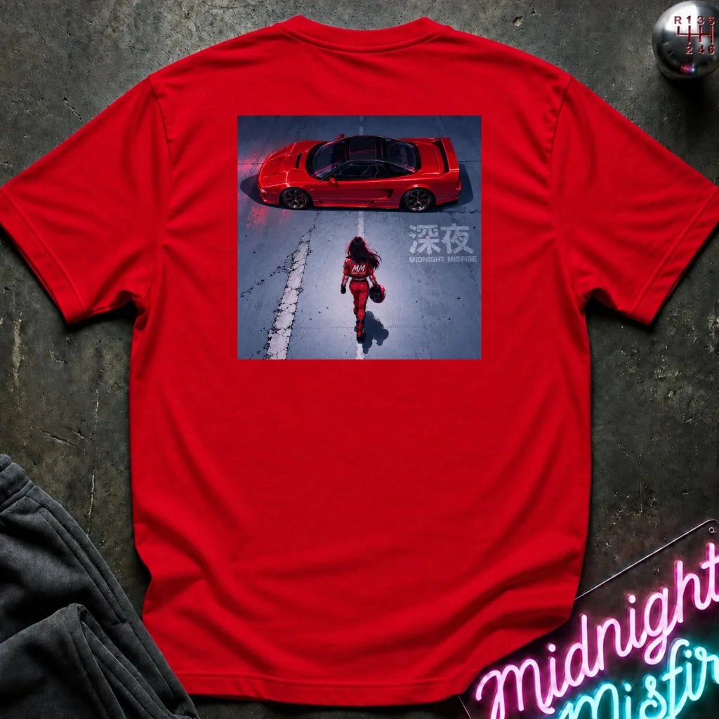 A bright red short-sleeve t-shirt laid flat on a dark textured surface, featuring a large square graphic print on the back with a red sports car and a woman walking in the snow. A neon sign and dark clothing are partially visible around the edges.