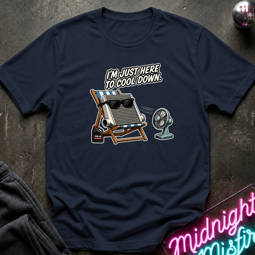 A navy blue graphic t-shirt laid flat on a dark textured surface. The graphic features a radiator sitting on white and blue striped beach chair and small fan, and the text 'I'M JUST HERE TO COOL DOWN.