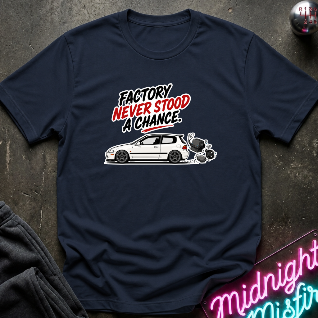 A navy blue graphic t-shirt laid flat on a dark textured surface. The shirt features a white car illustration and the text 'FACTORY NEVER STOOD A CHANCE' in black, white, and red.