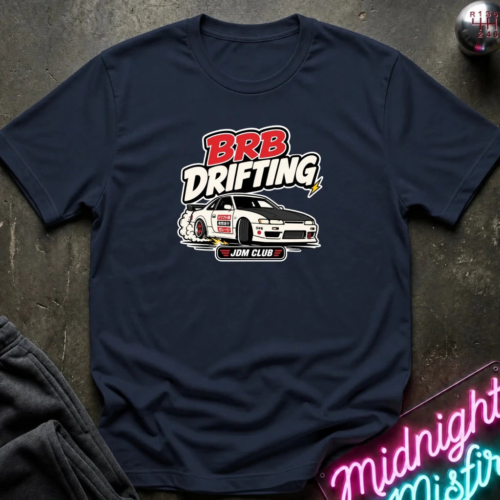 A navy blue graphic t-shirt laid flat on a dark textured surface. The shirt features a 'BRB DRIFTING' graphic 