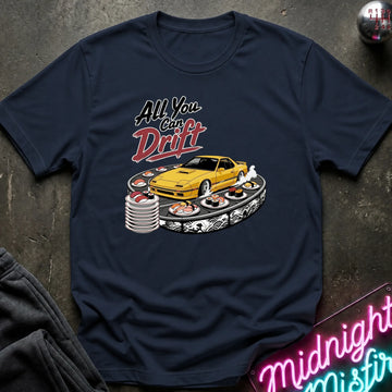A navy blue graphic t-shirt laid flat on a dark textured surface. The graphic features the text 'All You Can Drift' in stylized white and red lettering above a yellow sports car on a drift track with sushi plates.
