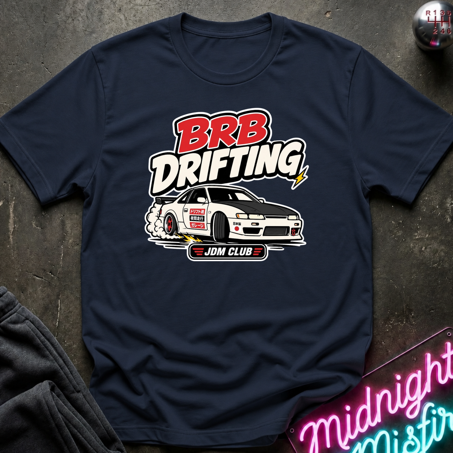 A navy blue graphic t-shirt laid flat on a dark textured surface. The shirt features a 'BRB Drifting' JDM Club car graphic in red, white, and black.