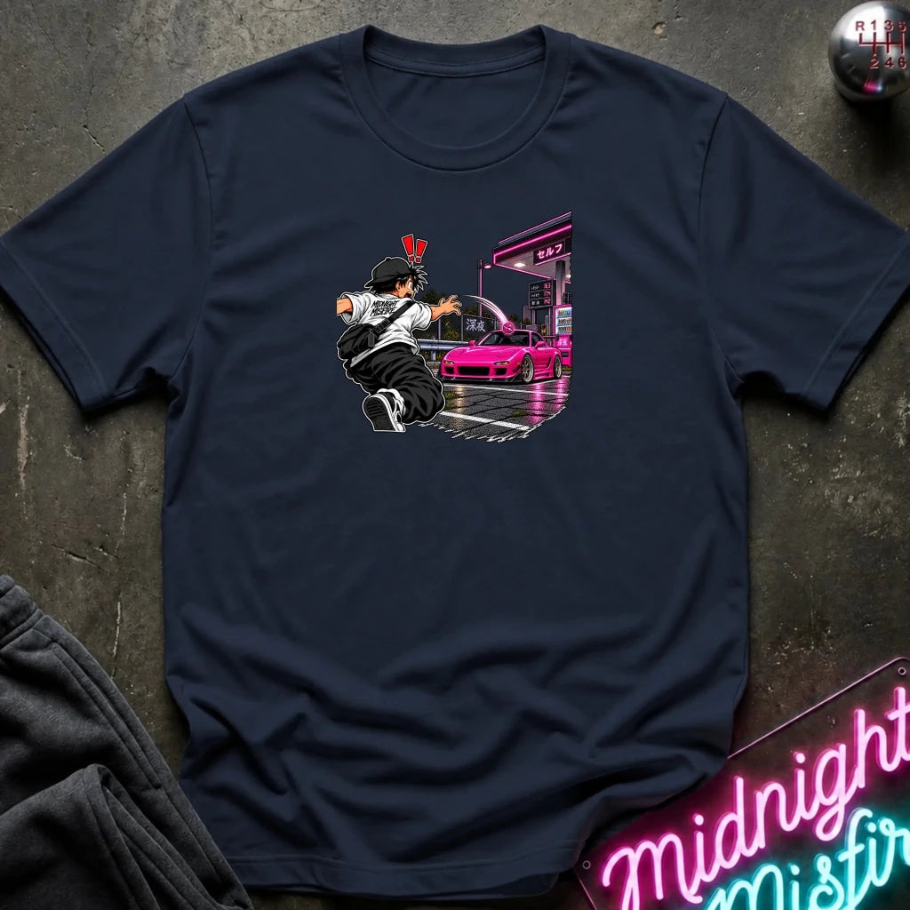 A navy blue short-sleeve crewneck t-shirt laid flat on a dark textured surface. The center of the shirt features a graphic print of an anime character in a black and white outfit with a hat, next to a sports car 
