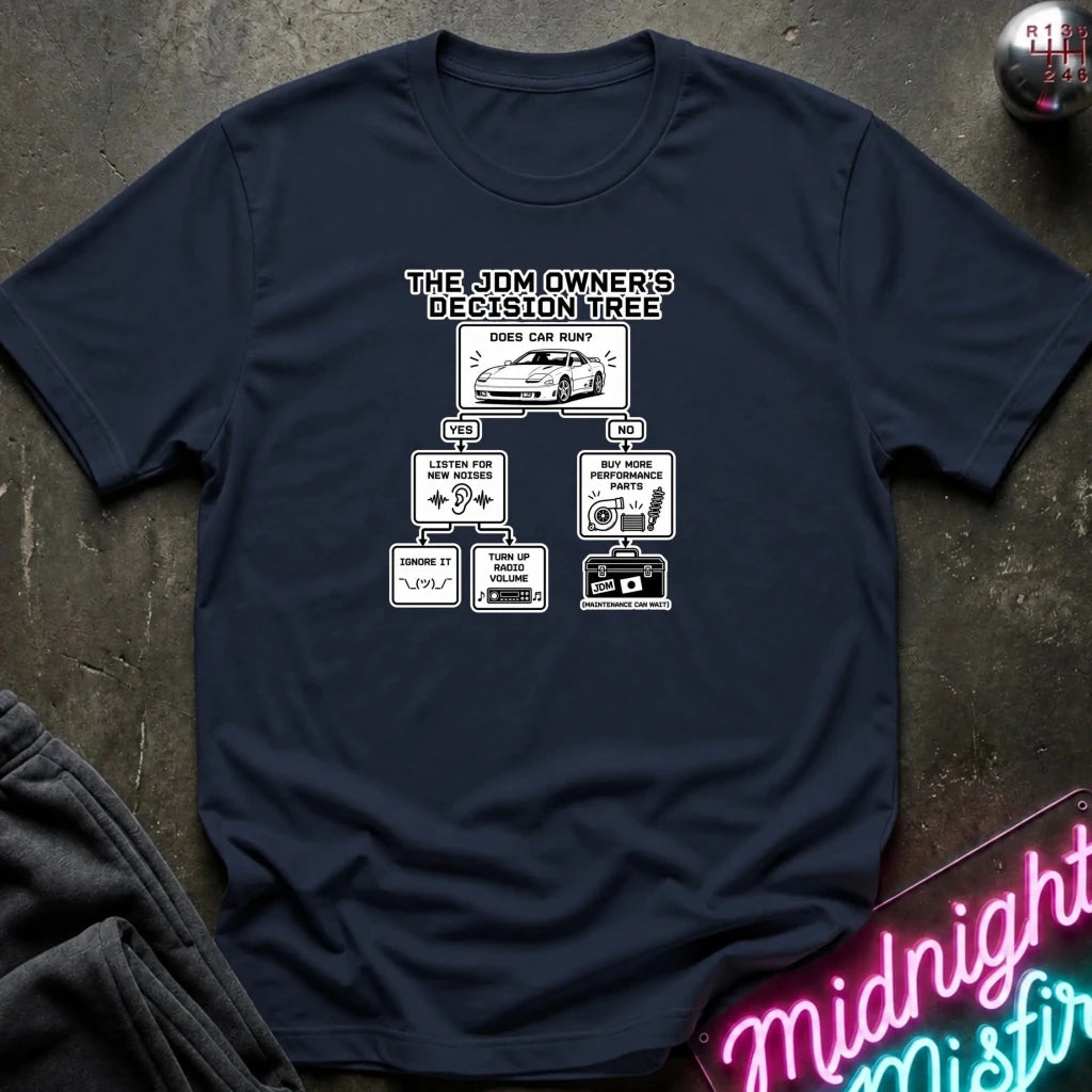 A navy blue graphic t-shirt laid flat on a dark textured surface. The shirt features a white printed graphic titled 'THE JDM OWNER'S DECISION TREE' with a car illustration and flow-chart boxes.