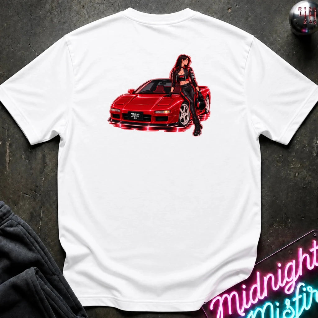 A white short-sleeve t-shirt laid flat on a dark textured surface, featuring a graphic print of a red sports car with a woman in a black outfit leaning on it. 