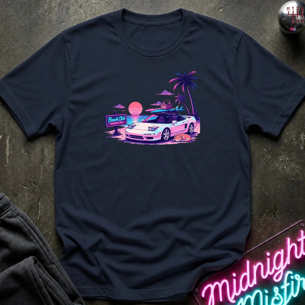 A navy blue short-sleeve t-shirt laid flat on a dark textured surface, featuring a colorful retro graphic of a white sports car on a beach with palm trees and a sunset.