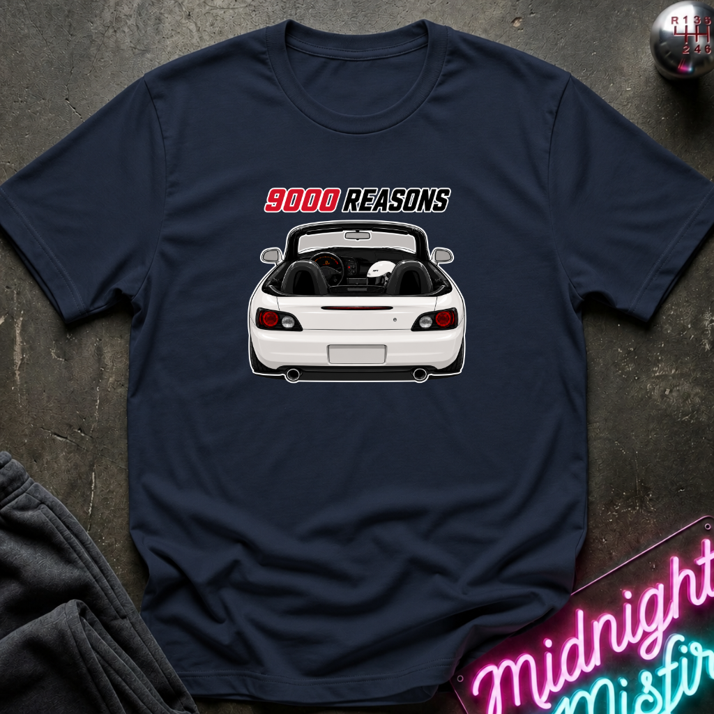 A navy blue short-sleeve t-shirt laid flat on a dark textured surface, featuring a graphic of a white convertible car with the text '9000 REASONS' above it. A neon sign and folded dark fabric are partially visible around the edges.