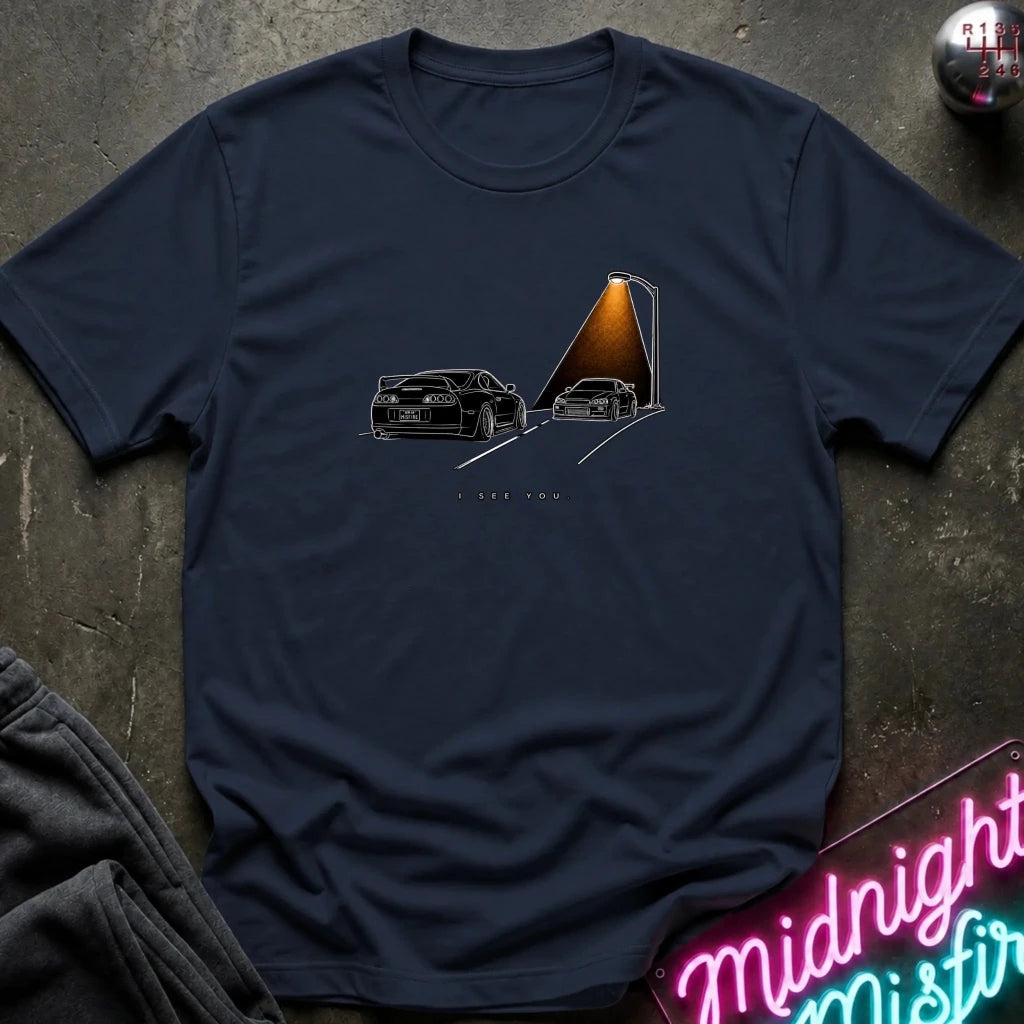 A navy blue short-sleeve t-shirt laid flat on a dark textured surface, featuring a graphic print of two black sports cars passing each other.