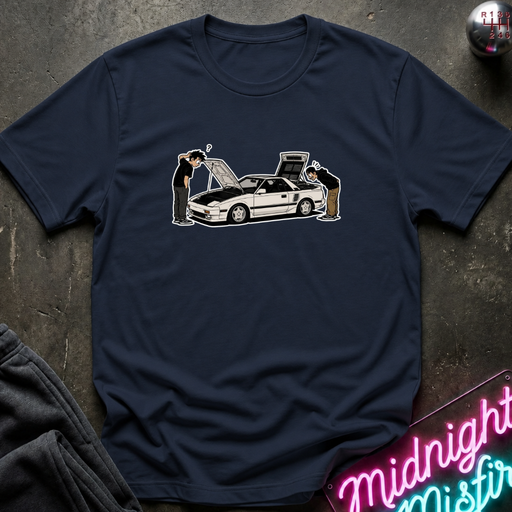 A navy blue short-sleeve t-shirt laid flat on a dark textured surface, featuring a graphic print of a white sports car with two people looking at it. A neon sign reading 'Midnight Mistir' is visible in the bottom right corner.