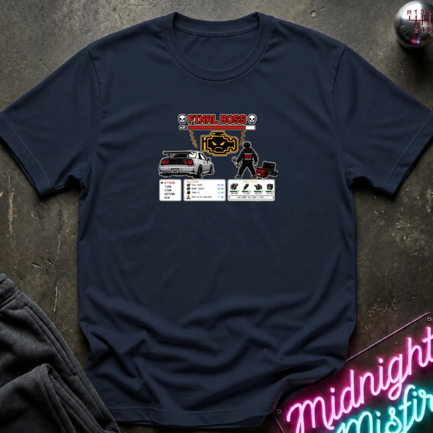 A navy short-sleeve crewneck t-shirt laid flat on a dark textured surface, featuring a central graphic print of a rpg character and a car. 